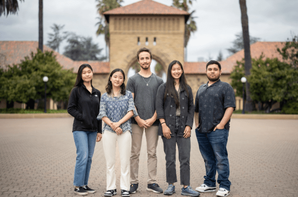 Five people stand in a row before an arch in Main Quad.